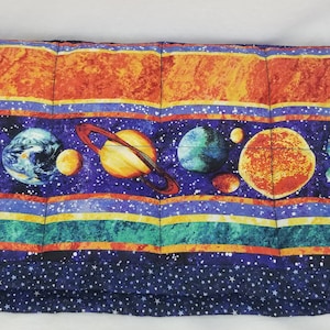 May include: A blue weighted blanket with a space theme. The blanket features a repeating pattern of planets, stars, and stripes in shades of orange, yellow, green, and blue.