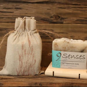 May include: A bar of Cool Peppermint Soap by 9 Senses, packaged in a natural fabric bag with a brown floral design. The soap is on a wooden soap dish.