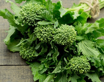 May include: A bunch of fresh green broccoli rabe, tied together with twine, on a wooden surface.
