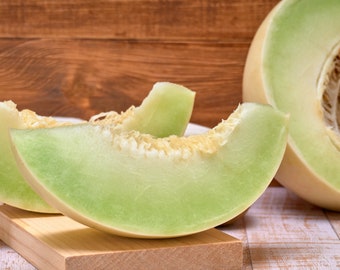 May include: A whole cantaloupe melon and three slices of cantaloupe melon on a wooden cutting board. The cantaloupe melon is light green and has a creamy white flesh. The melon slices are arranged on a wooden cutting board. There is a kiwi fruit in the background.