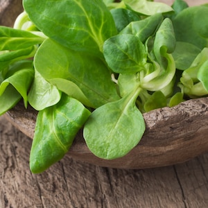 May include: A close-up of a wooden bowl filled with fresh, green lamb's lettuce.