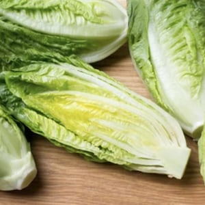 May include: Fresh romaine lettuce heads, with vibrant green outer leaves and pale yellow inner leaves, are arranged on a wooden surface. Some heads are whole, while others are cut, revealing the crisp texture.