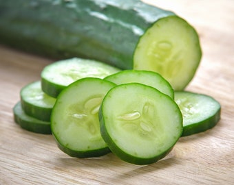 May include: A close-up of a wooden cutting board with several slices of fresh green cucumber. The cucumber slices are arranged in a circular pattern, with the largest slice in the center.