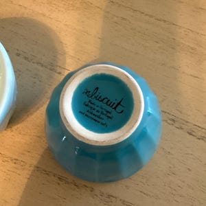 May include: A small, turquoise ceramic bowl with a ridged exterior. The bottom of the bowl has the word "biscuit" in cursive, along with text indicating it's made in Portugal, dishwasher and microwave safe.