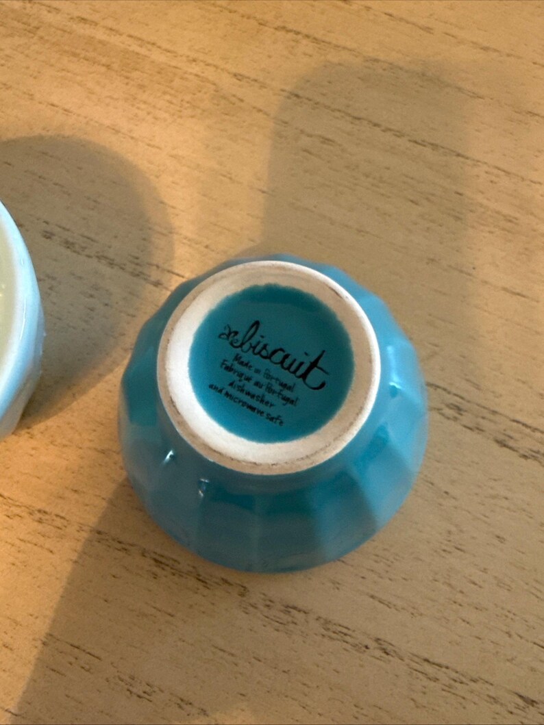 May include: A small, turquoise ceramic bowl with a ridged exterior. The bottom of the bowl has the word "biscuit" in cursive, along with text indicating it's made in Portugal, dishwasher and microwave safe.