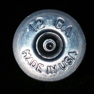 May include: A silver shotgun shell with the text "12 GA MADE IN USA" printed on it.
