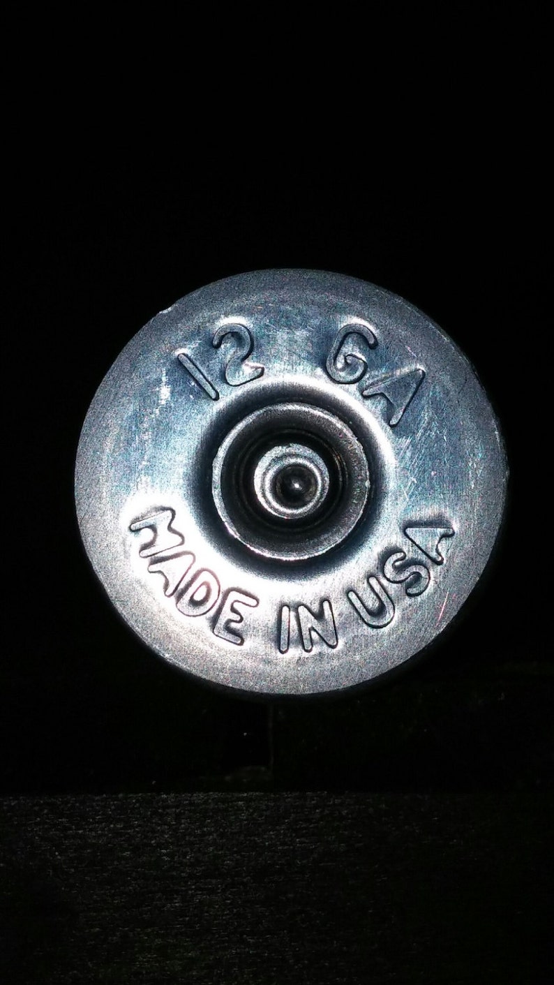 May include: A silver shotgun shell with the text "12 GA MADE IN USA" printed on it.