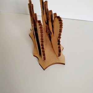May include: Wooden napkin holder with a decorative design. The holder is made of light brown wood and has a scalloped edge.