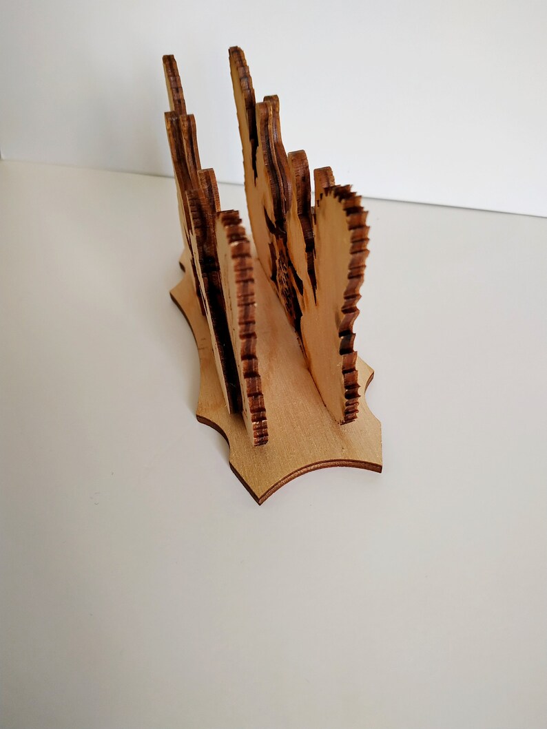 May include: Wooden napkin holder with a decorative design. The holder is made of light brown wood and has a scalloped edge.