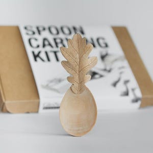 Peut inclure: Une cuillère en bois avec un motif de feuille de chêne, faisant partie d'un kit de sculpture de cuillère. La cuillère est brun clair, avec une sculpture de feuille détaillée. Le kit comprend une boîte en carton avec l'inscription "SPOON CARVING KIT".