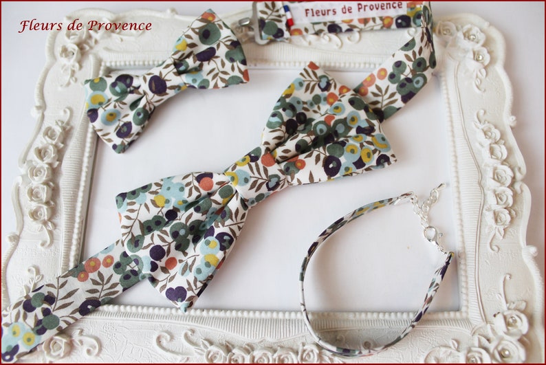 Puede incluir: Tres pajaritas a juego y una pulsera con un estampado floral. La tela es blanca con flores verdes, azules, amarillas y naranjas. Las pajaritas son de diferentes tama&ntilde;os. La pulsera est&aacute; hecha de tela y tiene un cierre plateado.