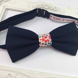 May include: A navy blue bow tie with a white and red floral pattern. The bow tie has a black adjustable strap with the text "FLEURS de PROVENCE" printed on it.