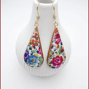 May include: Floral teardrop earrings with gold-coloured hooks and a brown border. The earrings feature a pattern of pink, blue, orange, and white flowers. The text "Fleurs de Provence" is at the bottom.