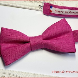 Op de afbeelding: Een felroze vlinderdas van textiel. De vlinderdas ligt op een witte achtergrond in een decoratieve lijst. De tekst "Fleurs de Provence" is zichtbaar op de band van de vlinderdas.