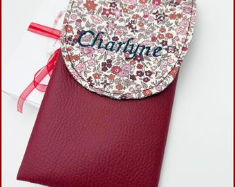 May include: A burgundy leather phone case with a white floral flap. The flap has the name "Charlyne" embroidered in dark blue thread. The case is labeled "Fleurs de Provence".