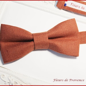 Peut inclure: Un nœud papillon en lin couleur rouille avec une sangle en tissu marron. Le nœud papillon est sur une surface blanche avec le texte "Fleurs de Provence" imprimé dessus.
