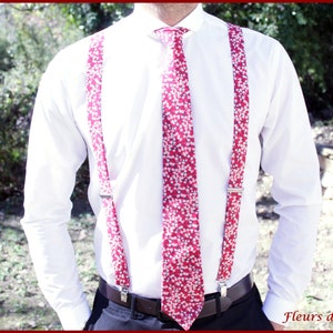 May include: A white dress shirt with a red floral patterned tie and suspenders. The suspenders and tie feature a repeating pattern of small white flowers on a red background. The suspenders have silver metal clips.