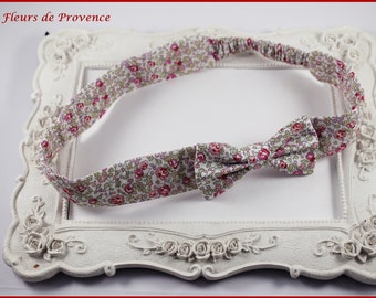 May include: A floral headband with a bow, featuring a pattern of small pink and white flowers on a light background. The headband is displayed on a white, ornate picture frame. The text "Fleurs de Provence" is in the top left corner.