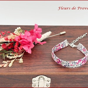 May include: A floral boutonniere with pink and red flowers, and a fabric bracelet with a floral pattern. The boutonniere has a pin. The bracelet has a silver chain and clasp. The text "Fleurs de Provence" is in the top right corner.