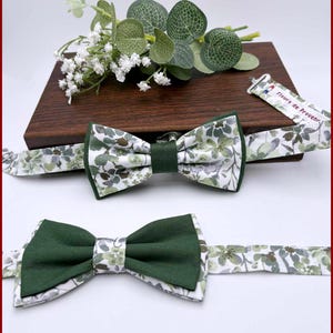 Può includere: Due papillon con motivo floreale e centro verde unito. I papillon sono esposti su una superficie di legno con vegetazione. Il testo "Fleurs de Provence" è in basso nell'immagine.
