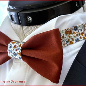 May include: A terracotta bow tie with a floral patterned centre, and a matching patterned collar band. The bow tie is set against a white shirt and a dark navy suit jacket. The text "Fleurs de Provence" is at the bottom.
