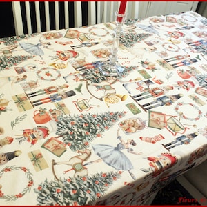 Peut inclure: Une nappe de Noël crème avec un motif de casse-noisettes, de sapins de Noël, de ballerines, de couronnes et de cadeaux. Un bougeoir en verre transparent avec une bougie rouge est sur la table.