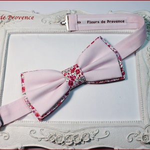 Könnte beinhalten: Hellrosa Fliege mit floral gemusterten Rändern und Mitte. Die Fliege ist vor einem weißen dekorativen Rahmen platziert. Der Text "Fleurs de Provence" ist auf dem Fliegenriemen zu sehen.