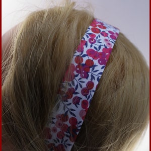 Könnte beinhalten: Ein weißes Stirnband mit einem Blumenmuster mit rosa und roten Blumen und blauen Blättern. Das Stirnband ist aus Stoff und hat ein schlichtes Design.