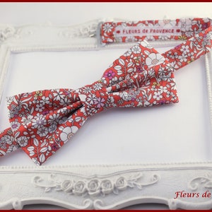 Peut inclure: Un nœud papillon rouge avec un motif floral blanc. Le nœud papillon est en tissu et a un design simple. Le nœud papillon est présenté sur un fond blanc avec un cadre décoratif.