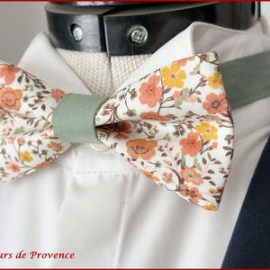 May include: A white bow tie with a floral pattern in shades of orange, yellow, and green. The bow tie has a green adjustable strap.