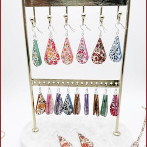 May include: A display of teardrop-shaped earrings in various floral patterns and colors, including pink, red, blue, and green. The earrings are suspended from a gold-colored metal earring stand. The text "Fleurs de Provence" is at the top.