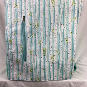 May include: A teal fabric with a white birch tree pattern and small green leaves. There are white birds with red beaks on the fabric. A zipper is visible on the left side of the fabric.