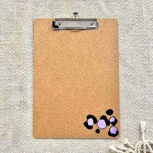 May include: A brown clipboard with a metal clip and a purple and black leopard print design in the bottom right corner.