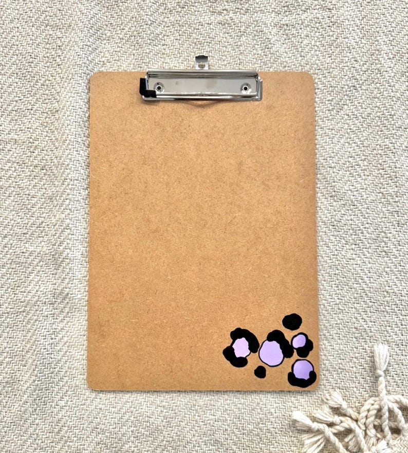 May include: A brown clipboard with a metal clip and a purple and black leopard print design in the bottom right corner.