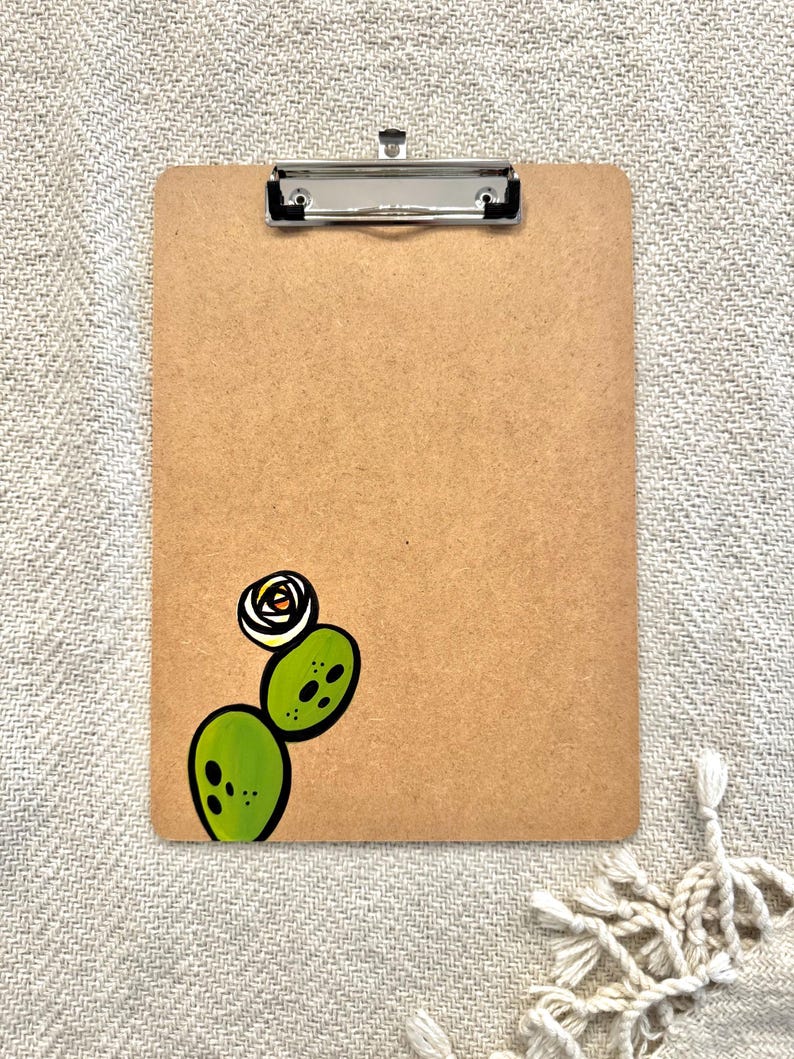 May include: A brown clipboard with a silver clip and a hand-painted green cactus with a white flower on the bottom right corner.