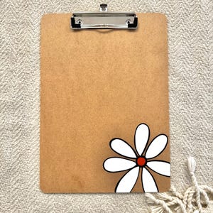 May include: A brown clipboard with a white daisy with a red center painted on the bottom right corner.