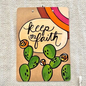 May include: A brown clipboard with a painted design featuring a cactus, flowers, and the text "keep the faith".