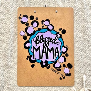 May include: A brown clipboard with a purple and blue design. The design features a circle with the words "Blessed Mama" and the text "Prov. 31:28".