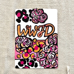 May include: A white background with the text "WWJD" in gold and pink lettering. The text is surrounded by pink and white roses and black and pink leopard print.