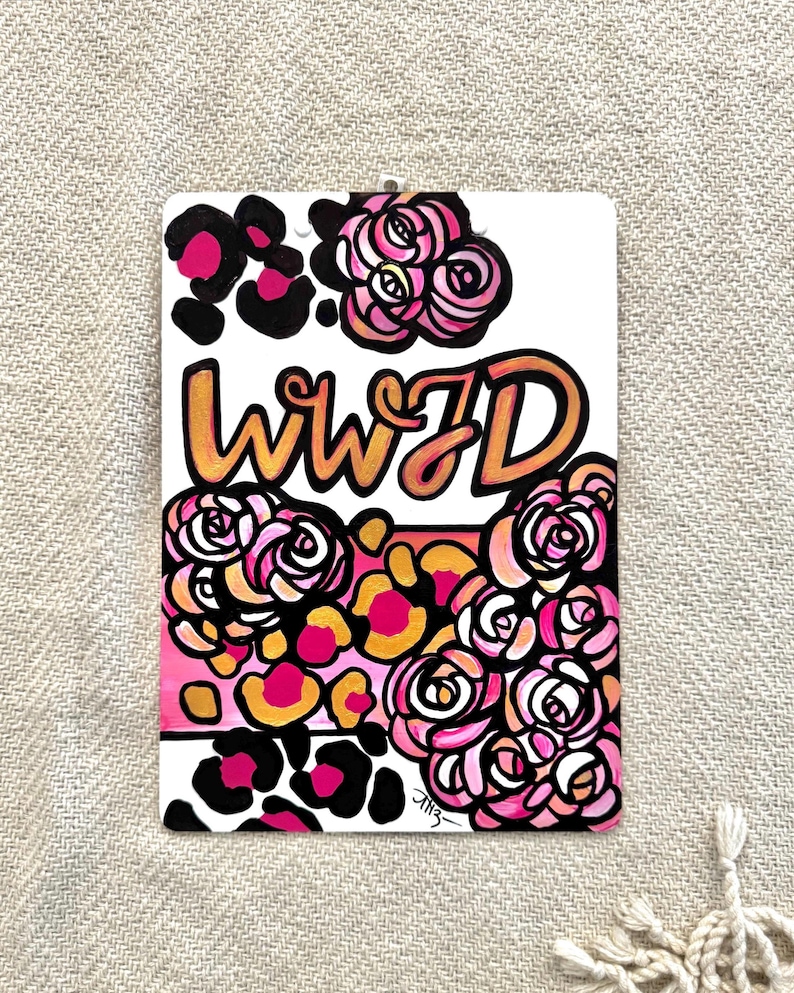 May include: A white background with the text "WWJD" in gold and pink lettering. The text is surrounded by pink and white roses and black and pink leopard print.