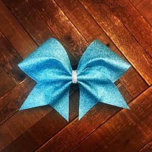 May include: A large, bright blue glitter cheer bow with a silver rhinestone in the center.