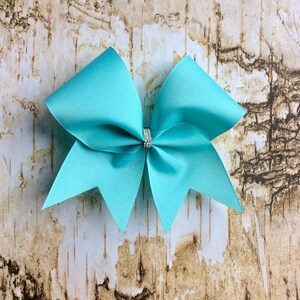 May include: A large turquoise bow with a sparkly rhinestone center. The bow is made of a soft, shiny fabric and is perfect for adding a touch of sparkle to any outfit.