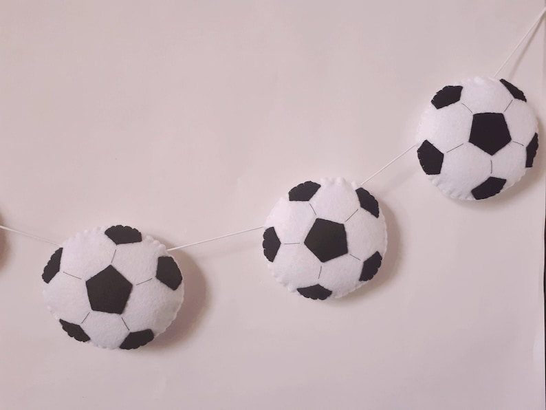 Puede incluir: Una guirnalda de bolas de f&uacute;tbol de fieltro blanco y negro con cinco bolas de f&uacute;tbol colgando de una cuerda blanca.