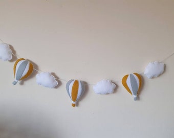 May include: A garland of felt hot air balloons and clouds in shades of grey and yellow. The garland is strung on a white string and is perfect for a nursery or child's room.