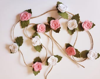 May include: A garland of felt flowers with pink and white roses and green leaves. The garland is strung on twine.