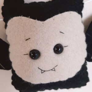 May include: A felt vampire decoration with a white face, black hair, and large black button eyes. The vampire has a stitched smile with two small fangs. It is likely part of a Halloween or spooky-themed craft project.
