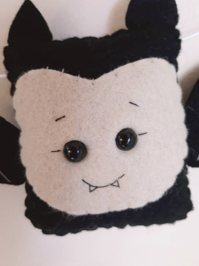 May include: A felt vampire decoration with a white face, black hair, and large black button eyes. The vampire has a stitched smile with two small fangs. It is likely part of a Halloween or spooky-themed craft project.
