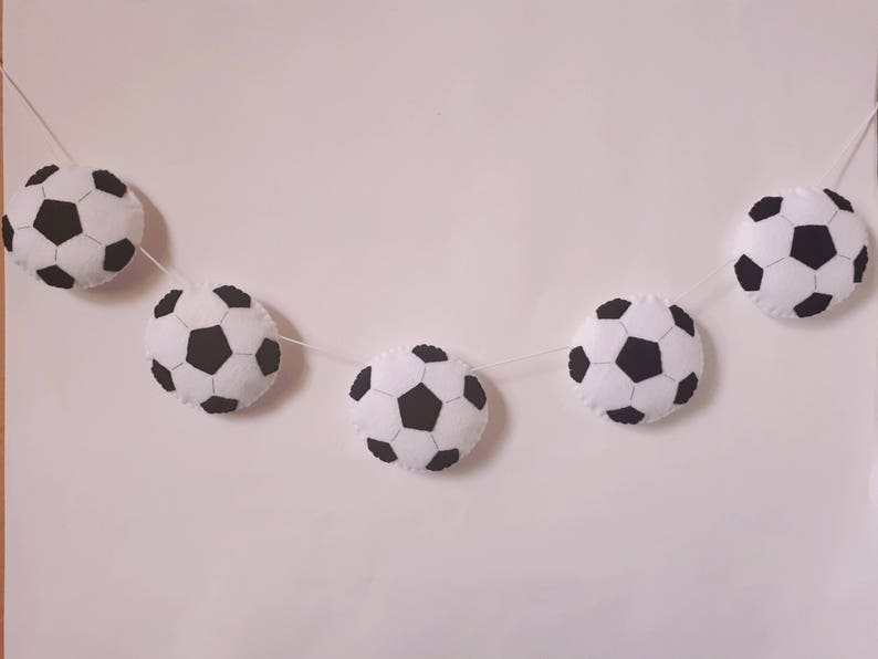 Puede incluir: Una guirnalda de balones de f&uacute;tbol blancos y negros con cinco balones de f&uacute;tbol de fieltro enhebrados en una cuerda blanca.
