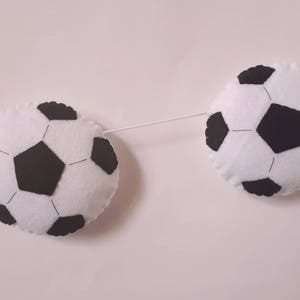Puede incluir: Una guirnalda de balones de f&uacute;tbol de fieltro blanco y negro con dos balones de f&uacute;tbol colgando de una cuerda blanca.