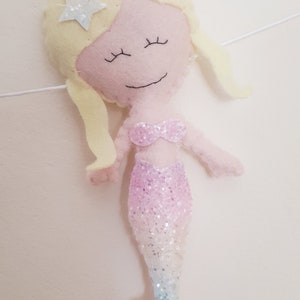 May include: A pink felt mermaid with a sparkly tail and blonde hair. The mermaid has a star on her head and closed eyes.